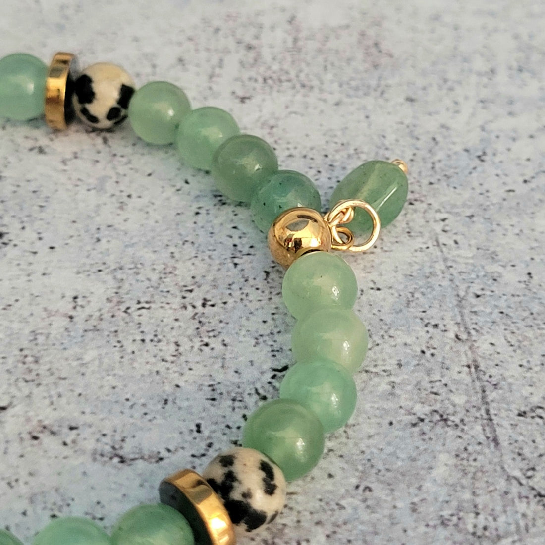 Détail de le breloque qui compose le bracelet. Bracelet femme aux jolies couleurs pastels. Composé de pierres semi-précieuses en aventurine verte, jaspe dalmatien et rondelles d'hématite dorées.